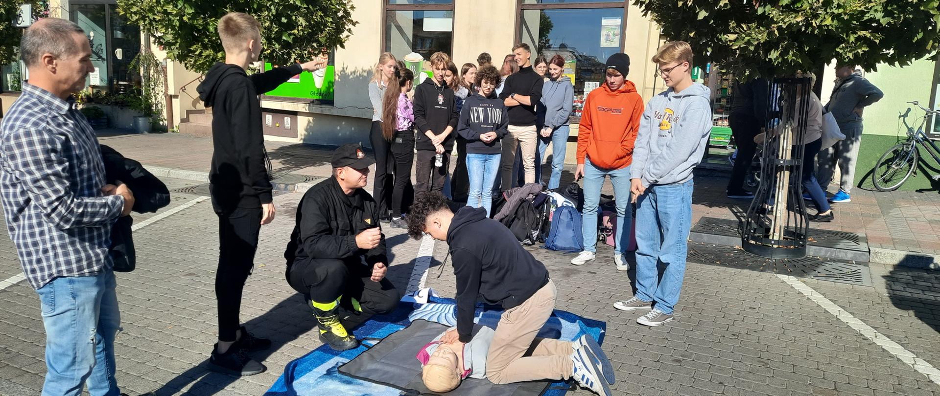 Na zdjęciu młodzież biorąca udział w akcji oraz strażak udzielający instruktażu