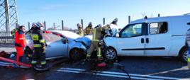 Zderzenie czołowe dwóch samochodów osobowych, obok strażacy oraz ratownik medyczny.