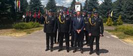 strażacy i starosta kozienicki stoją w szeregu, w tle poczty sztandarowe