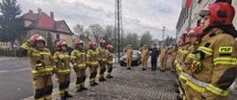 Zdjęcie przedstawia strażaków podczas uroczystej zmiany służbowej z okazji podniesienia flagi państwowej.