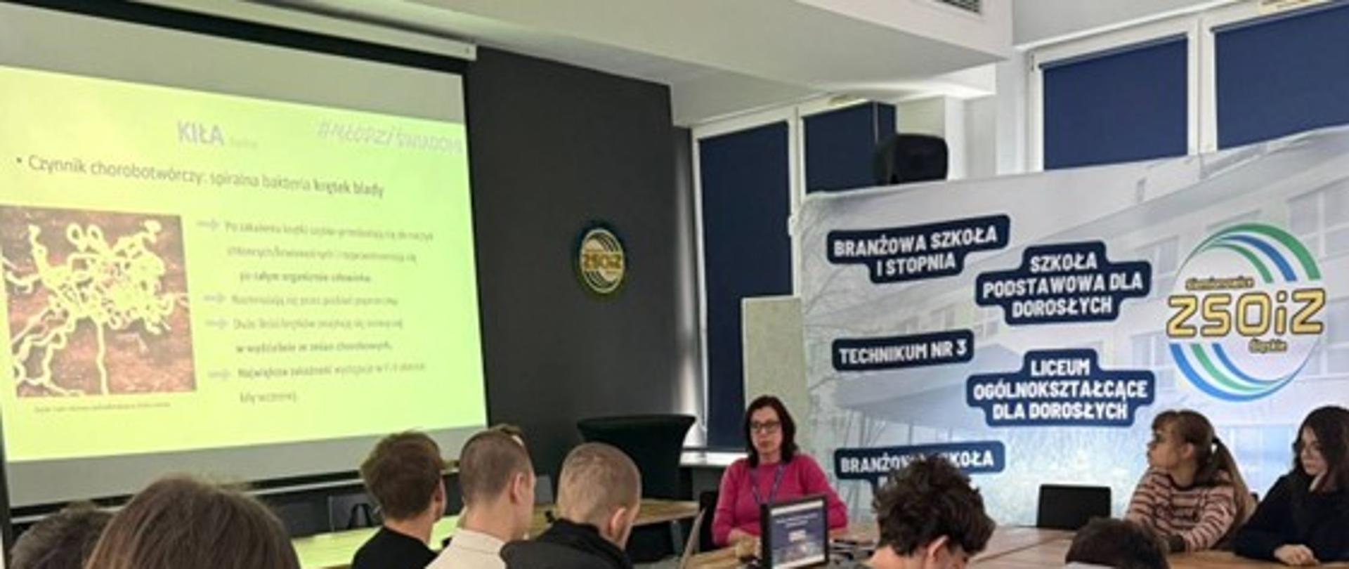 pracownik Inspekcji oraz grupa młodzieży szkolnej w trakcie spotkania na temat programu Młodzi Świadomi i chorób przenoszonych drogą płciową