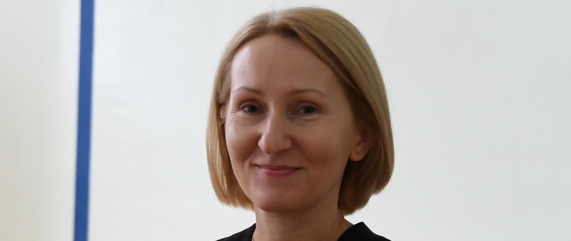 Kobieta lekko się uśmiecha, w ręku trzyma bukiet róż