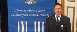 Odznaczony strażak na tle niebieskiego baneru Honorowy Dawca Krwi 