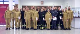 Pamiątkowe zdjęcie grupowe funkcjonariuszy i funkcjonariuszek PSP będących uczestnikami szkolenie CBRNE (19 osób) w towarzystwie Zastępcy Komendanta Centralnej Szkoły PSP, kobiety oraz trzech oficerów CS PSP