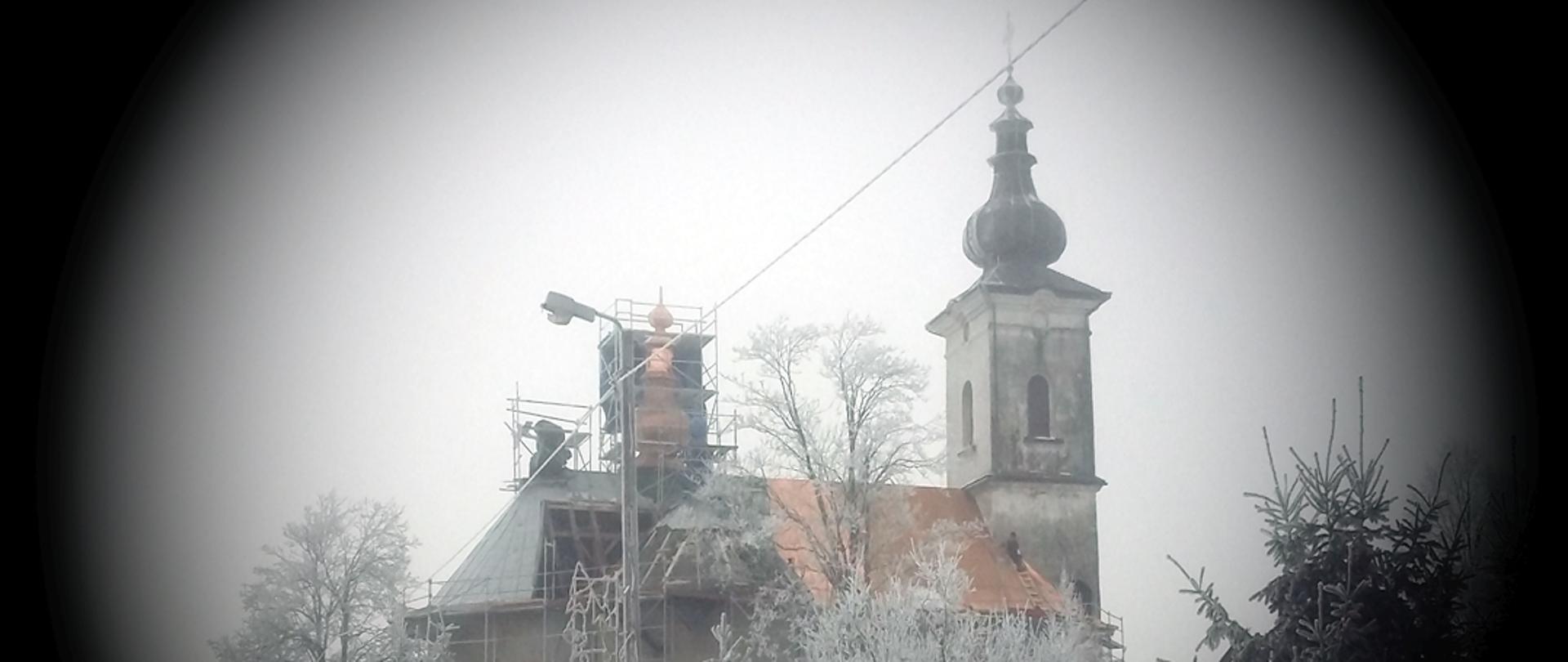 Widok na bok kościoła podczas remontu. Widoczne są rusztowania na wieżyczce dachowej części dachu. Rogi zdjęcia przyciemnione tworzą kolistą ramkę wokół budynku.