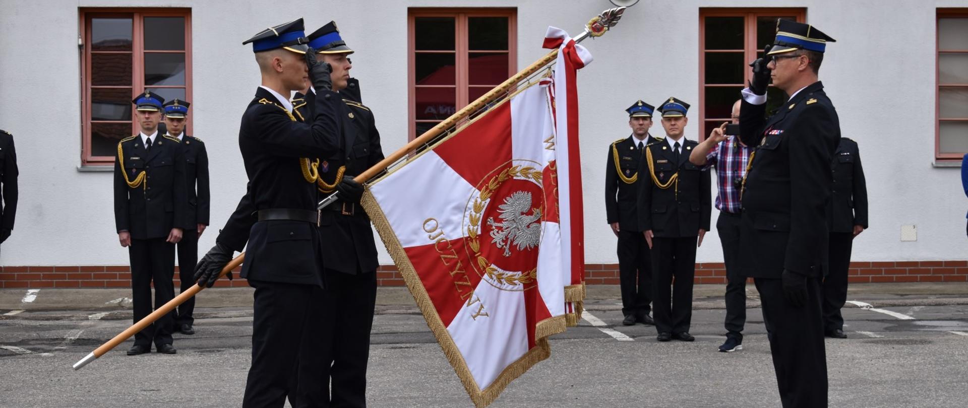 Zdjęcie przedstawia mł. bryg. Jarosława Gryciuka przed pocztem sztandarowym
