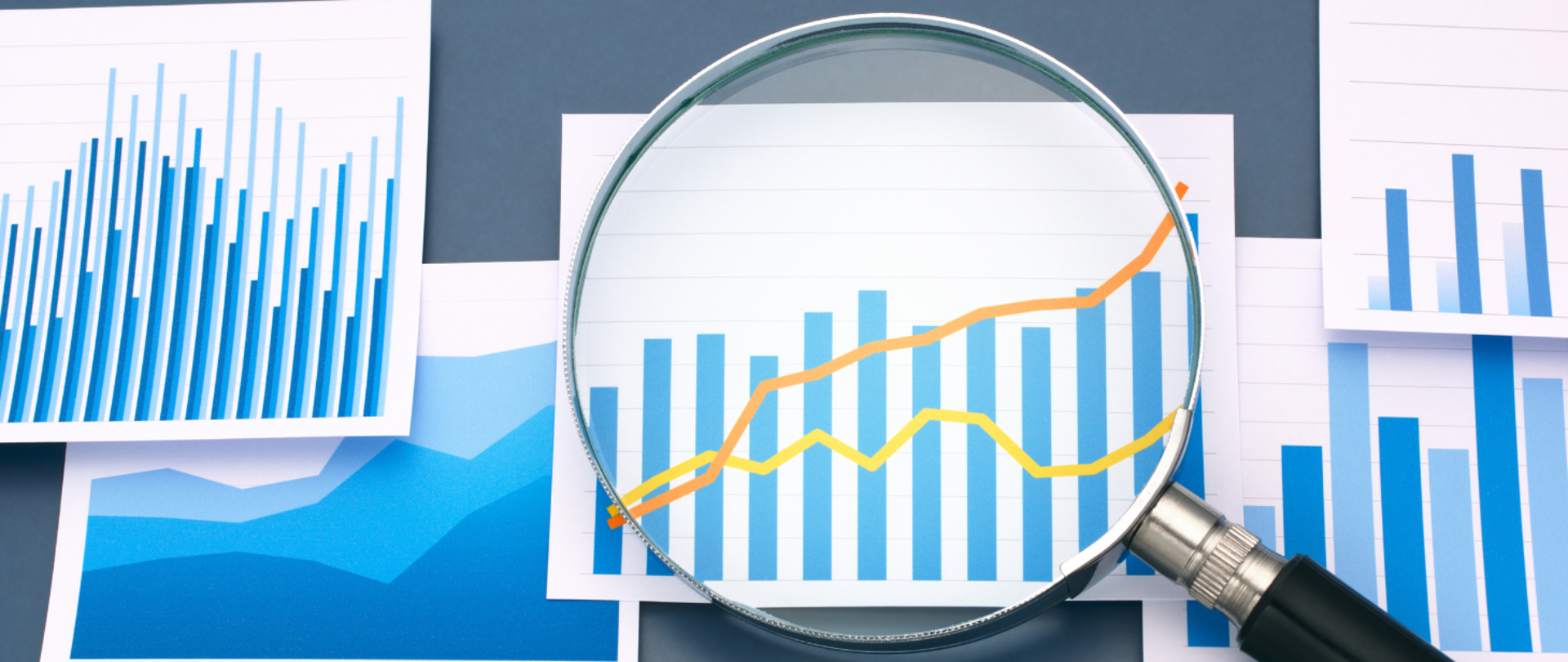 Lupa a pod nią różne wykresy na kartkach.