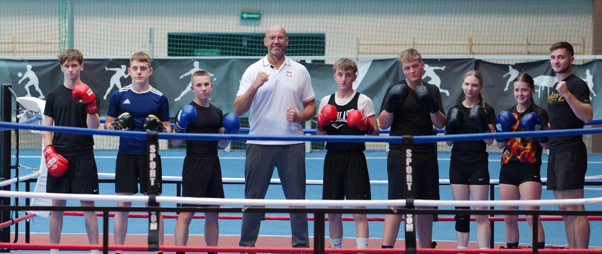 Minister Rutnicki z wizytą u RKS Łódź. Stoi na ringi z młodymi zawodnikami na sali gimnastycznej