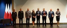 Wyróżnieni funkcjonariusze, osoby cywilne stoją wraz z prezesem Rady Ministrów stoją trzymając wyróżnienia po lewej stronie stoją trzy flagi Polski. 