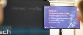 Stoisko MF i KAS na govtech, telebim z prezentacją konkursu na robota do walki z cyberprzestępczością