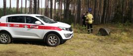 Na zdjęciu z lewej strony samochód operacyjny Komendy Powiatowej Państwowej Straży Pożarnej w Świeciu. Z prawej strony samochodu dwóch funkcjonariuszy Komendy Powiatowej Państwowej Straży Pożarnej w Świeciu sprawdzając oznakowanie punktu czerpania wody w lesie.