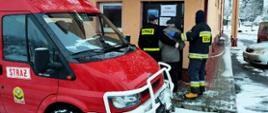 Na zdjęciu widać na pierwszym planie, po lewej stronie strażackiego osobowego busa. Na drugim planie dwóch strażaków pomaga seniorowi wejść do punktu szczepień