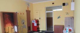 Na zdjęciu wyposażenie sali edukacyjnej w sprzęty użytku domowego. Z lewej otwarte drzwi za kturymi namalowany jest pożar mieszkania. Dalej namalowany pożar sadzy w kominie oraz dymek w kształcie potworka 