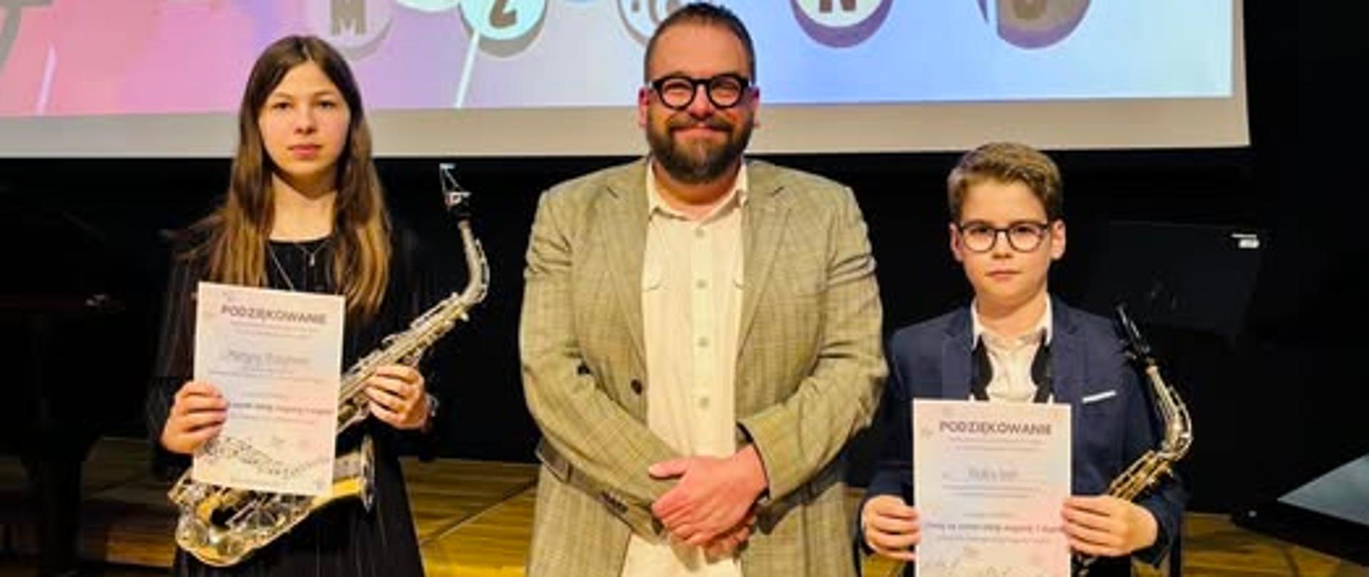 Dwoje saksofonistów razem z nauczycielem na scenie szkoły muzycznej w Rybniku