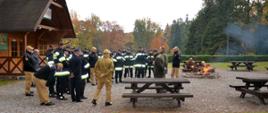 Leśniczy Arboretum Wirty omawia charakterystykę parku strażakom Państwowej Straży Pożarnej, niedaleko pali się ognisko. 