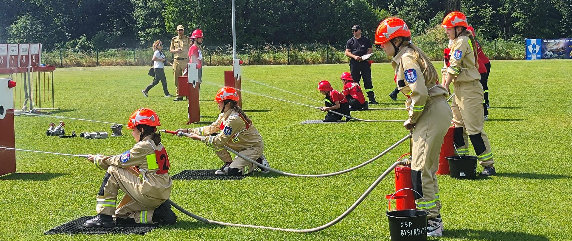 na zdjęciu widać młodzież podczas zawodów sportowo-pożarniczych. Dziewczynki na pierwszym planie leją wodę z hydronetek do tarcz.