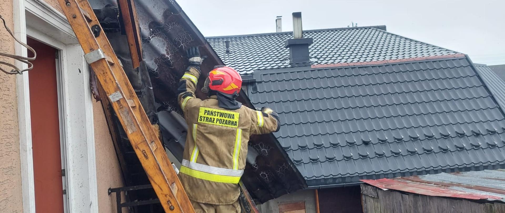 Na zdjęciu widoczny strażak podczas zdejmowania blachy z dachu