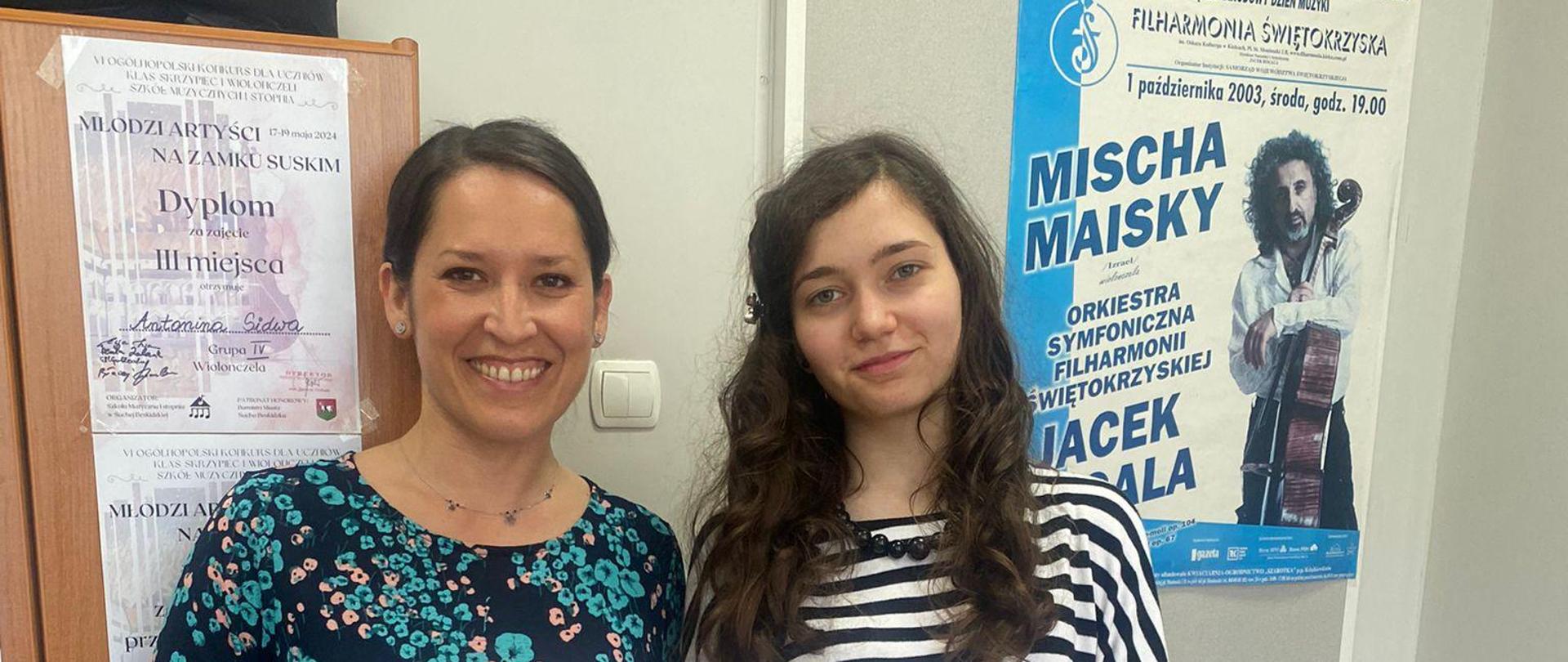 Zdjęcie przedstawia nauczycielkę i uczennicę stojące z dyplomami w rękach w tle widać szafę oraz drzwi wejściowe do sali lekcyjnej