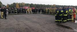 Na płycie leśnego lotniska stoją w dwuszeregu w kształcie litery U strażacy biorący udział w ćwiczeniach. Przemawia do nich Komendant Powiatowy Państwowej Straży Pożarnej w Świeciu starszy brygadier Piotr Tkaczyński.