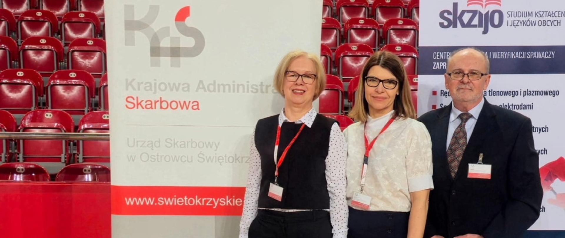 Trzy osoby stoją na tle banera i pozują do zdjęcia