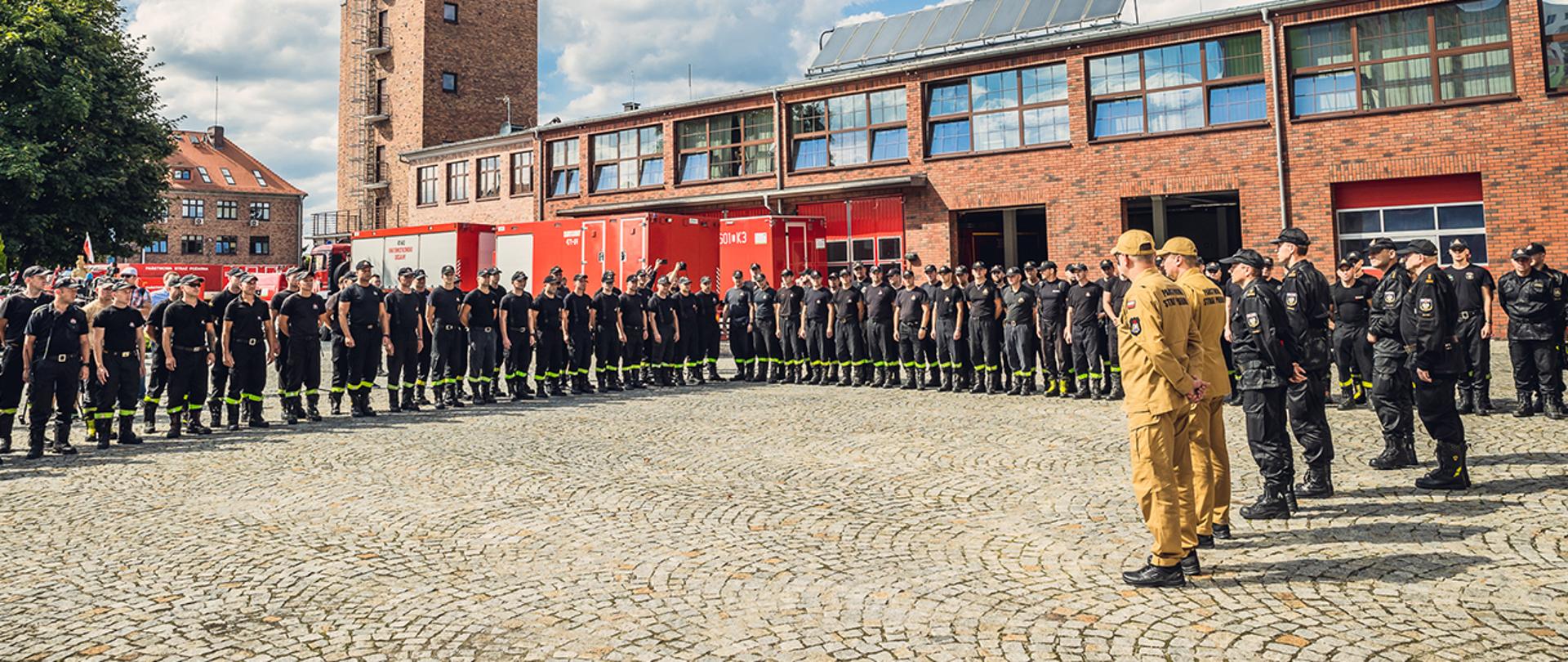 Strażacy stojący na placu Komendy Wojewódzkiej PSP we Wrocławiu podczas odprawy.