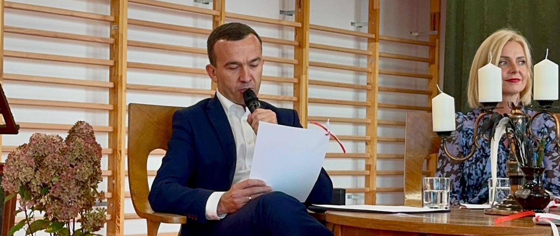 Mężczyzna siedzi i czyta z kartki 