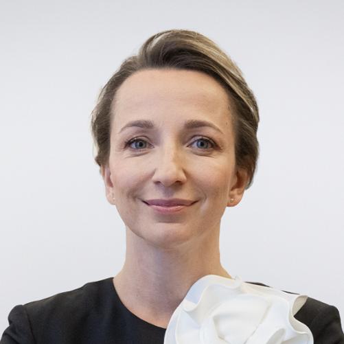 Portret Sylwii Gregorczyk-Abram - uśmiechnięta kobieta w sukience z założonymi rękoma