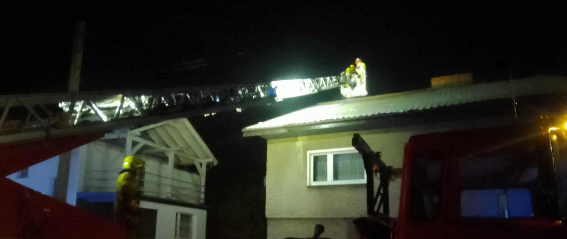 Na zdjęciu znajduje się samochód strażacki - drabina, w tle widać budynek jednorodzinny