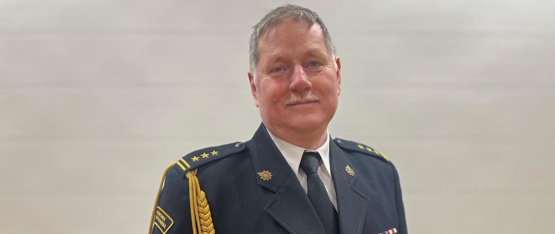 Funkcjonariusz Państwowej Straży Pożarnej w mundurze galowym na tle białej ściany