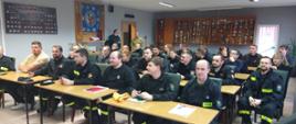 Na zdjęciu znajdują się druhowie OSP siedzący za ławkami na sali wykładowej, w tle stoi strażak
