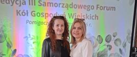 Na pierwszym planie widoczne są dwie uczestniczki wydarzenia, stojące przed ekranem z graficzną planszą promującą Forum. Tło stanowi dekoracyjna oprawa wizualna w jasnych barwach, z motywem roślinnym oraz wyraźnym napisem informującym o nazwie i edycji wydarzenia.