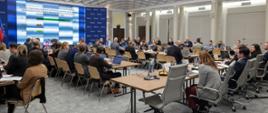 Na zdjęciu widać salę konferencyjną wypełnioną uczestnikami, siedzą przy stołach.