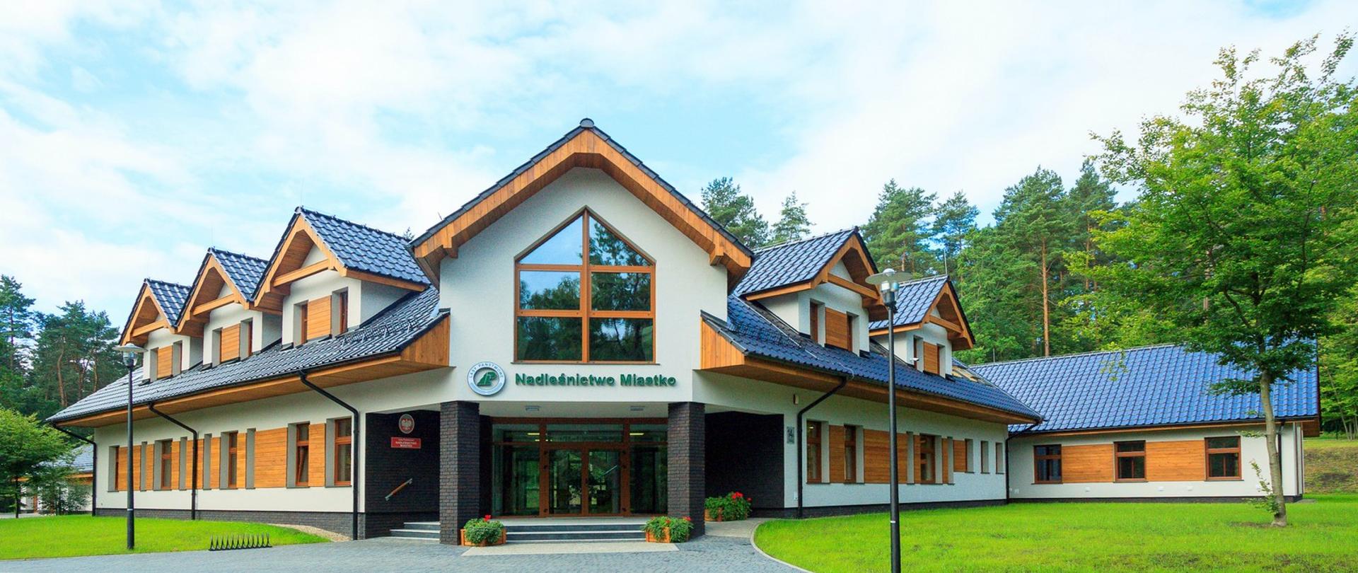Zdjęcie budynku, w którym znajduje się siedziba Nadleśnictwa Miastko. W sąsiedztwie budynku widać drzewa.