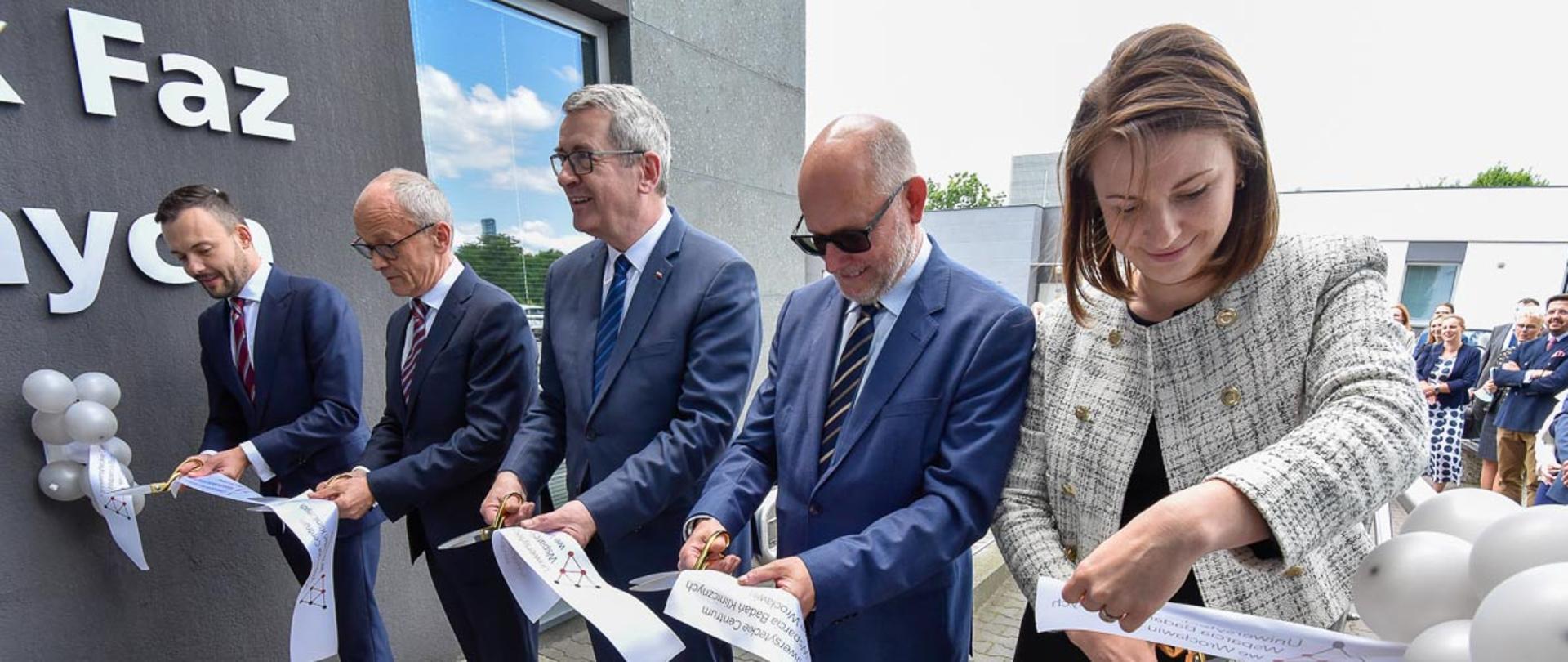 Grupa osób przecinających wstęgę. W środku wiceminister Murdzek, na pierwszym planie kobieta w jasnym żakiecie i czarnej spódnicy. 