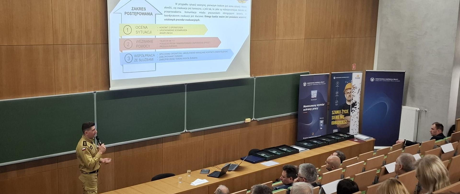 Strażak z mikrofonem stojący za biurkiem na auli wykładowej