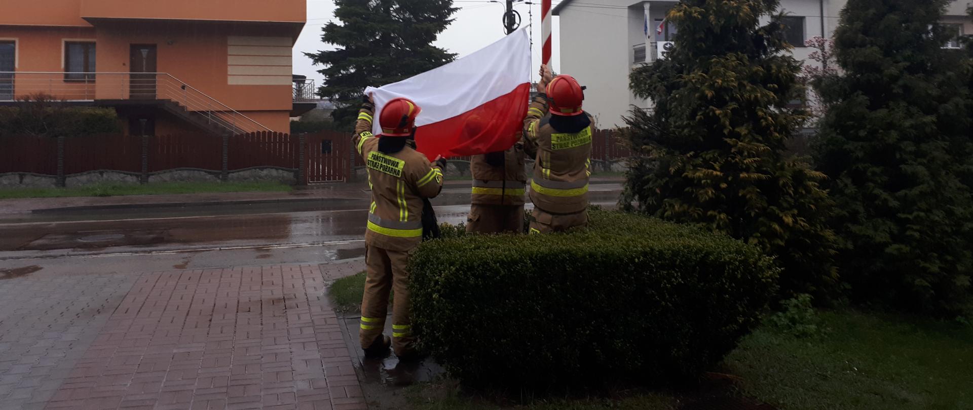 Zdjęcie przedstawia strażaków wieszających biało-czerwoną flagę
