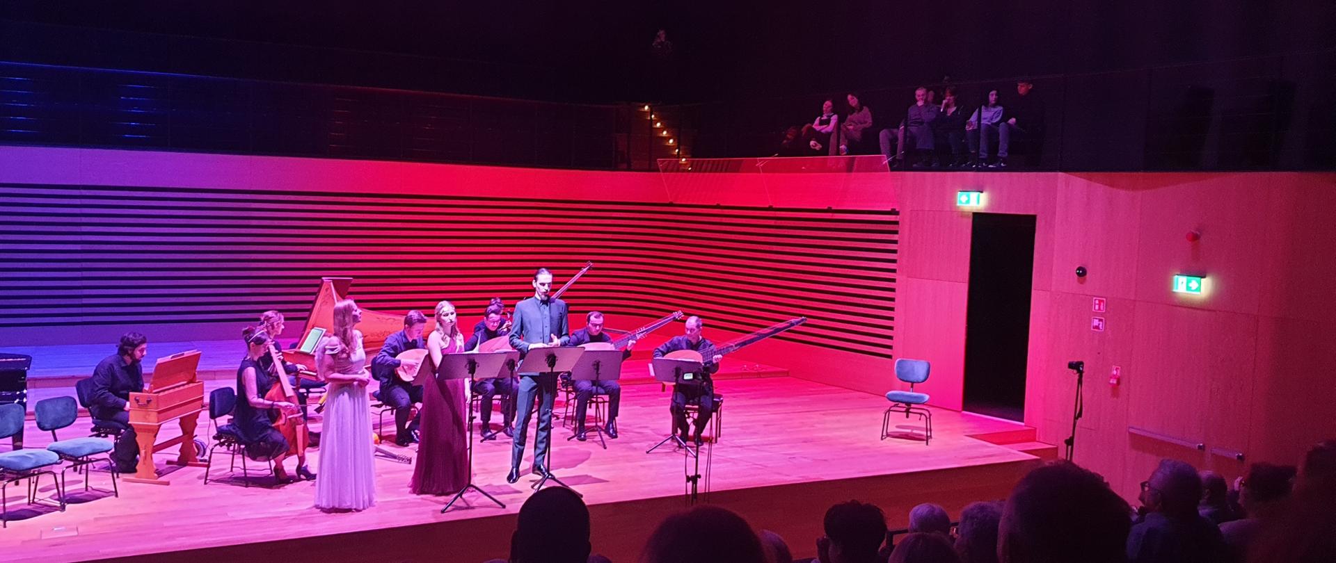 Grający zespół instrumentalny (7 muzyków), dwie śpiewające wokalistki i wokalista na scenie sali koncertowej PSM