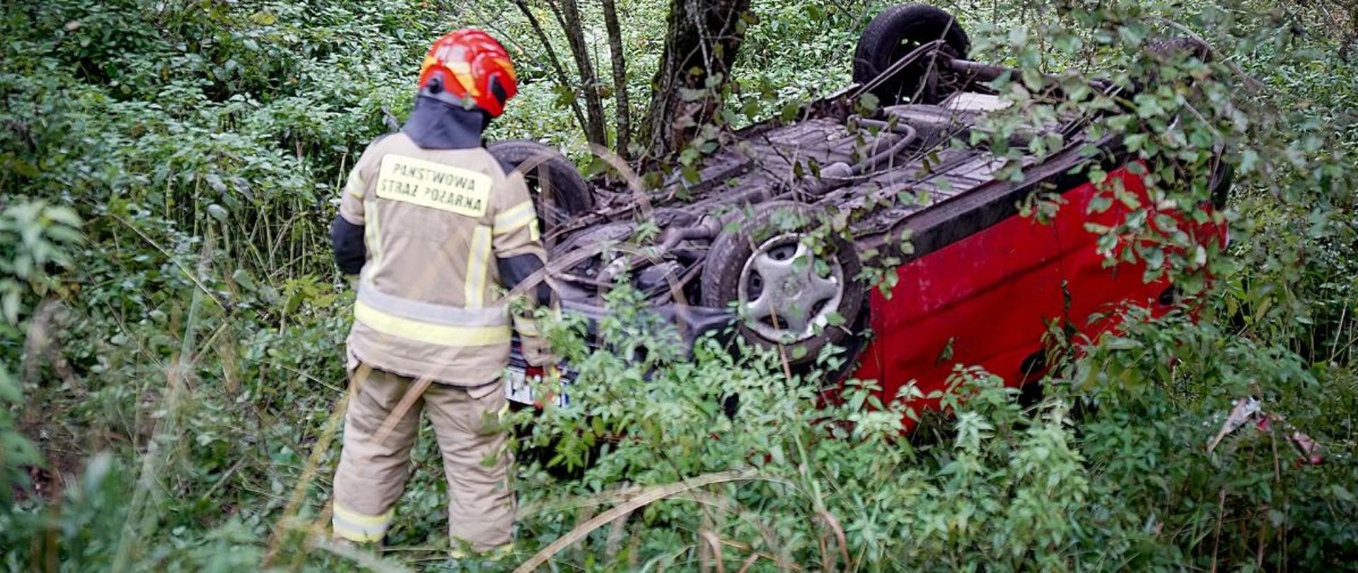 Zdjęcie przedstawia strażaka przy samochodzie który leży na dachu.
