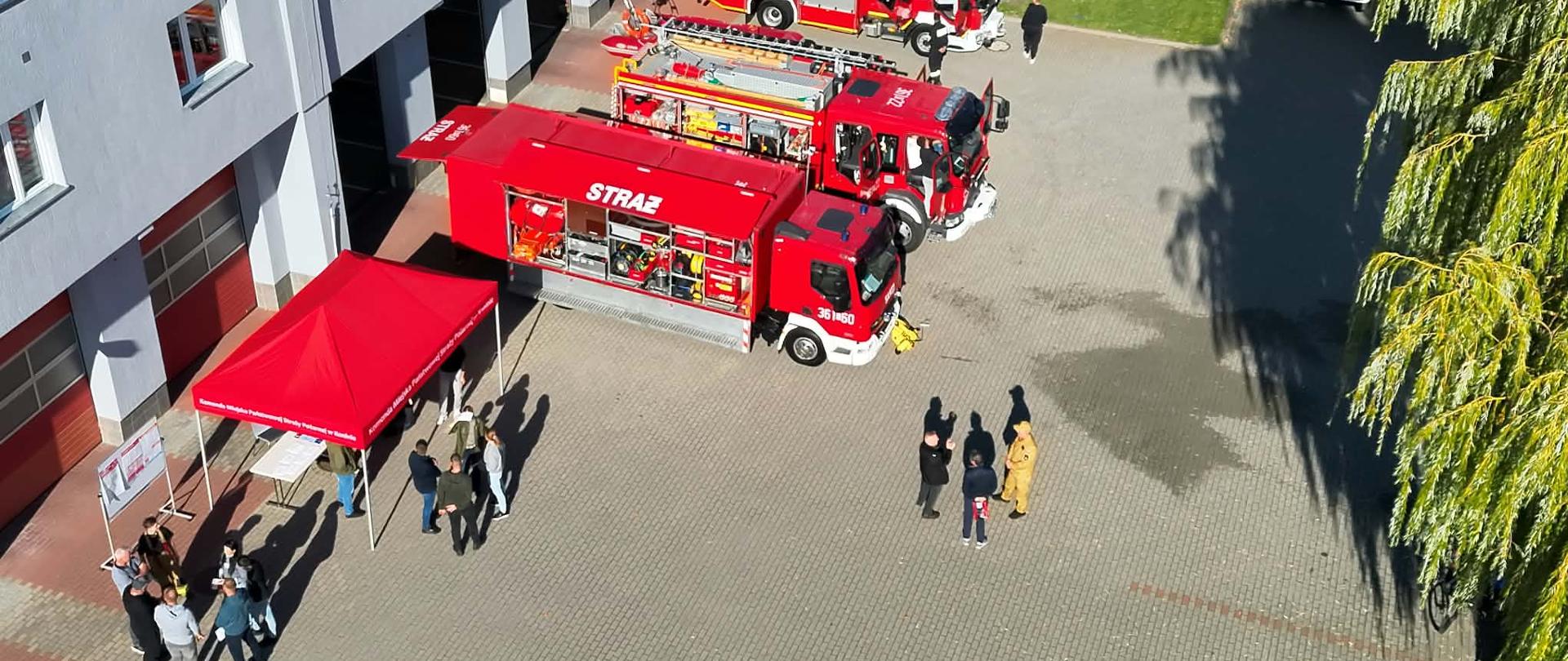 Zdjęcie wykonane z drona. Na placu przed komendą widać zaparkowane samochody strażackie, namiot oraz osoby które przyszły na trening rodzinny 