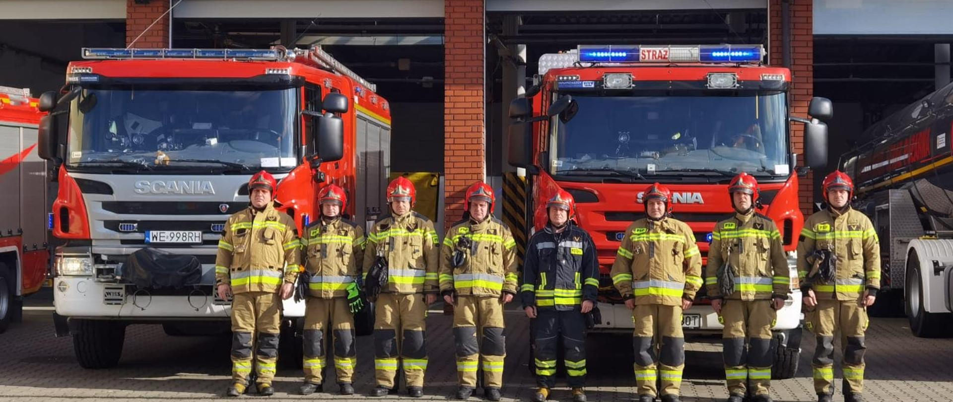 Strażacy stojący przed samochodami wystawionymi na plan wewnętrzny