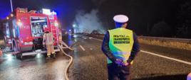 Funkcjonariusze Inspekcji Transportu Drogowego pomagają w zabezpieczeniu miejsca akcji ratownicz-gaśniczej na autostradzie A4 w Zabrzu. Z samochodów gaśniczych Straży Pożarnej są rozwinięte węże gaśnicze i podają wodę na palącą się ciężarówkę.