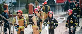 Strażacy na schodach budynku szkoły rozwijają linie gaśniczą
