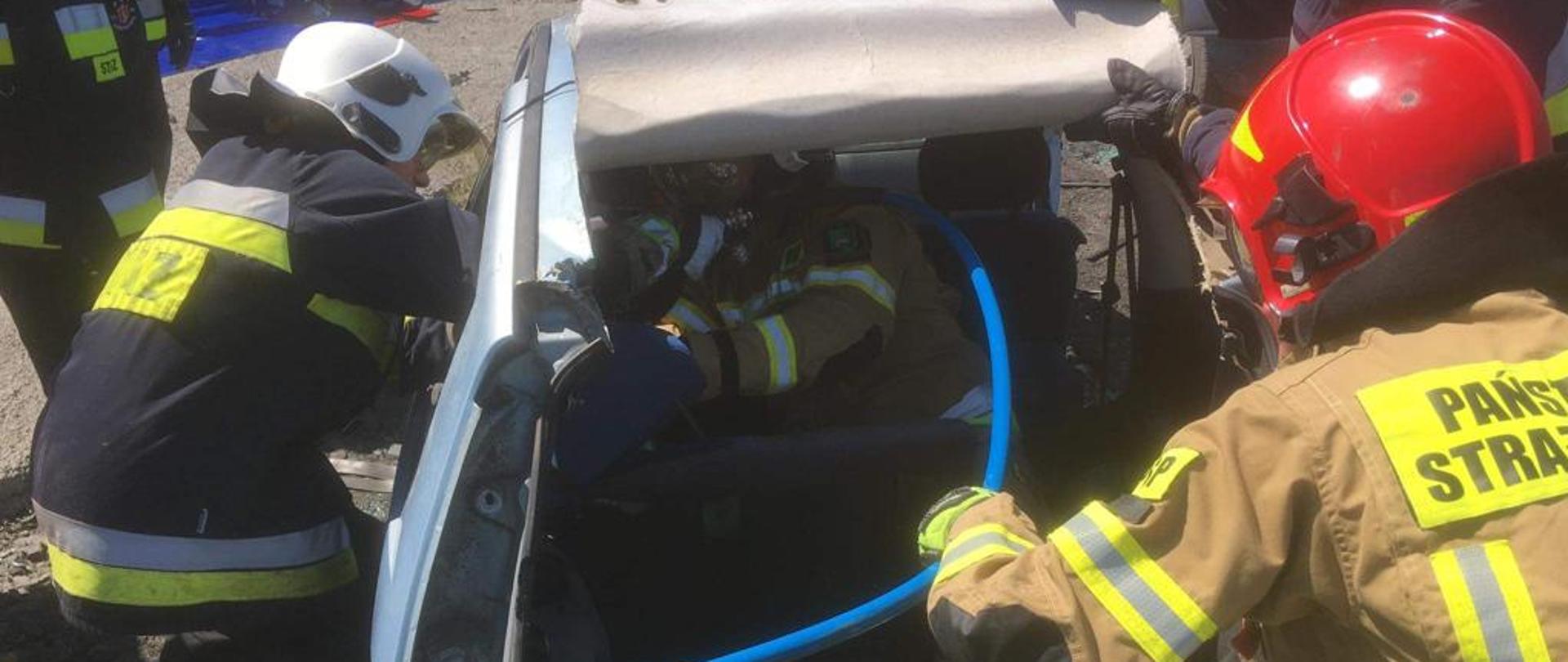 Zdjęcie przedstawia strażaków przy uszkodzonym samochodzie - ćwiczenia na złomowisku