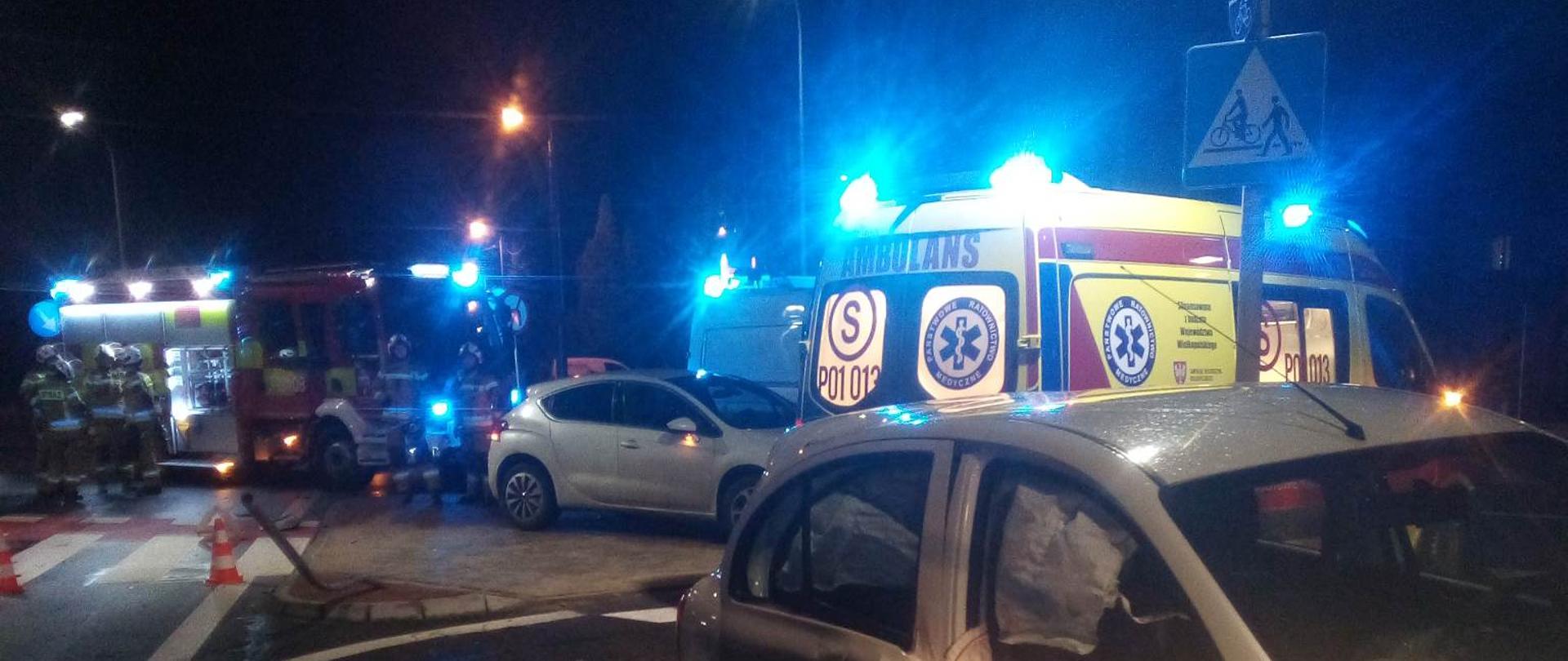 Zdjęcie w porze nocnej. Widać uszkodzony pojazd. Oświetlenie sztuczne. Na zdjęciu widać pojazd ratowniczo-gaśniczy z sygnalizacją ostrzegawczą, niebieską.
