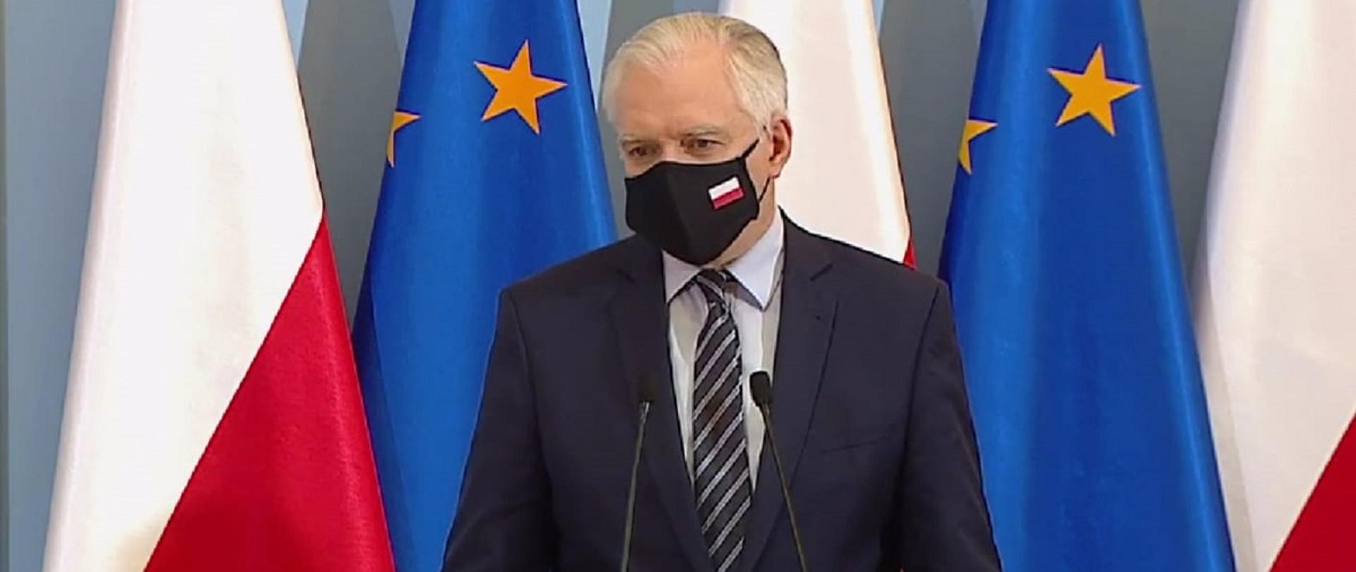 Wicepremier, minister rozwoju, pracy i technologii Jarosław Gowin, stojący przy mównicy z mikrofonami, z tłu flagi Polski i UE