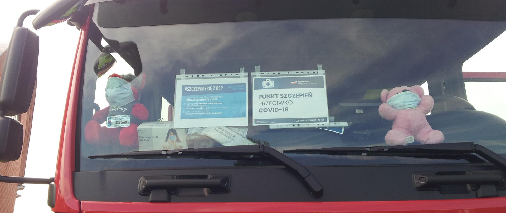 Przednia szyba pojazdu strażackiego a na niej przyklejone informacje odnośnie punktu szczepień.