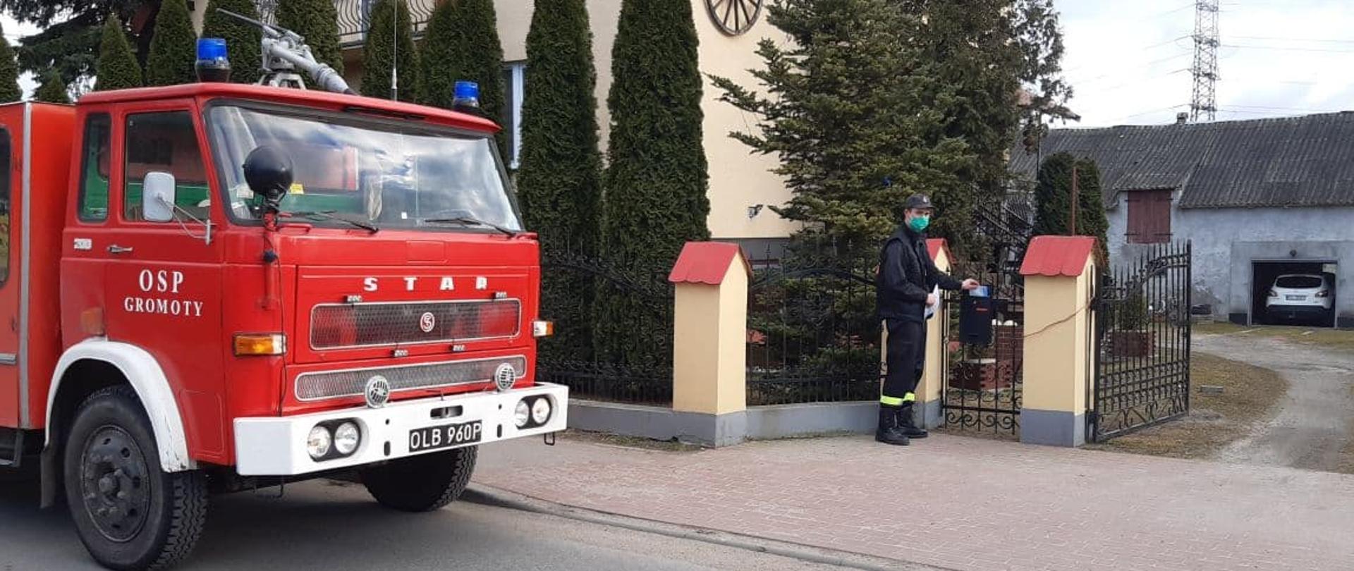 Strażak umieszczający ulotkę w skrzynce pocztowej przy jednej z posesji.