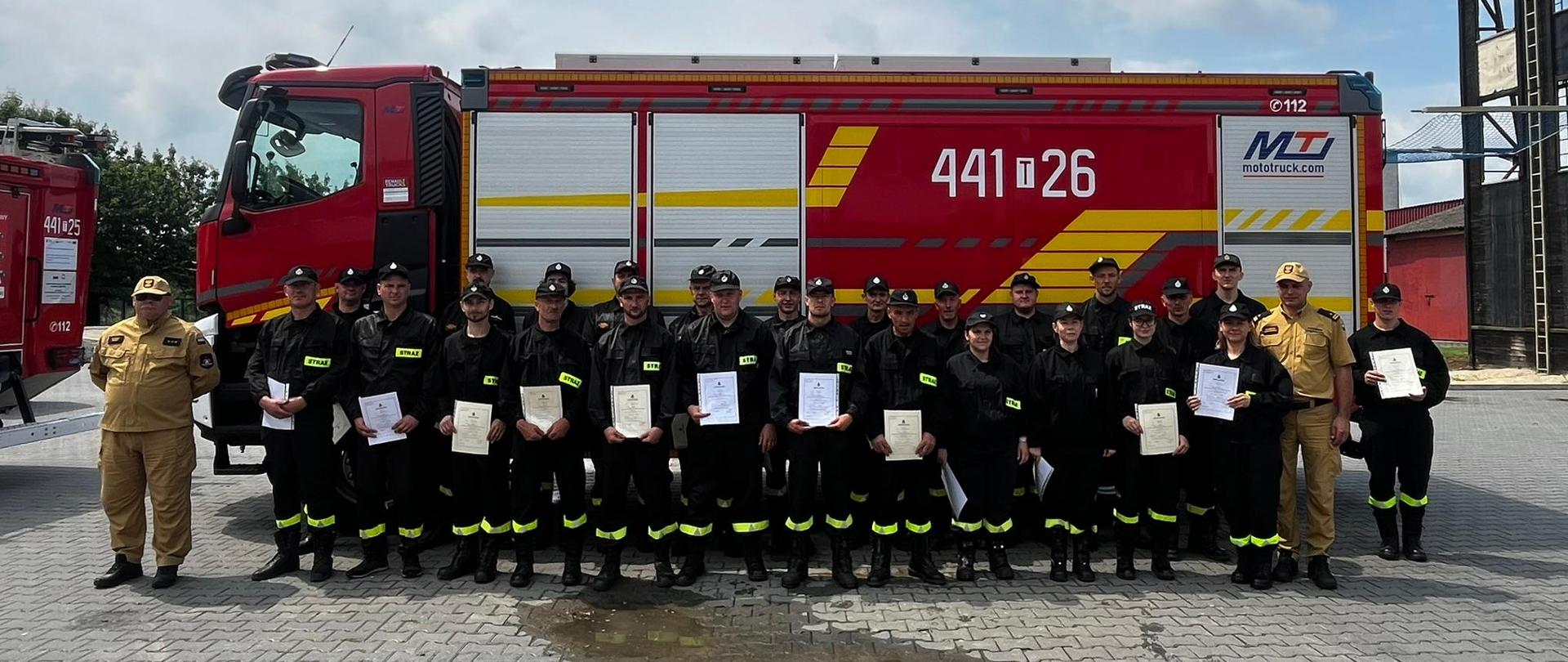 Strażacy OSP stojący na tle samochodu pożarniczego z zaświadczeniami ukończenia kursu.