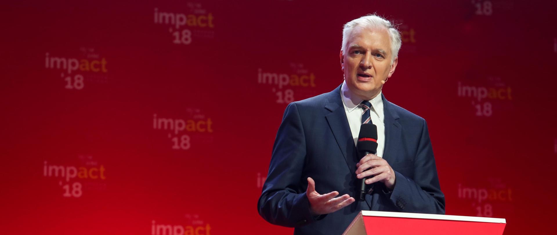 Minister Gowin przemawia, za nim czerwona ściana z napisami Impact'18