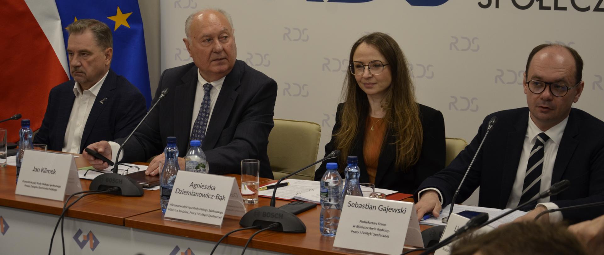 Na zdjęciu widnieje stół prezydialny za którym siedzą od lewej strony: Przewodniczący NSZZ „Solidarność” – Piotr Duda, Jan Klimek – Przewodniczący Rady Dialogu Społecznego, Agnieszka Dziemianowicz-Bąk 0 Ministra Rodziny, Pracy i Polityki Społecznej, Sebastian Gajewski – Podsekretarz Stanu w Ministerstwie Ministra Rodziny, Pracy i Polityki Społecznej. W tle siedzących baner z napisem Rada Dialogu Społecznego.